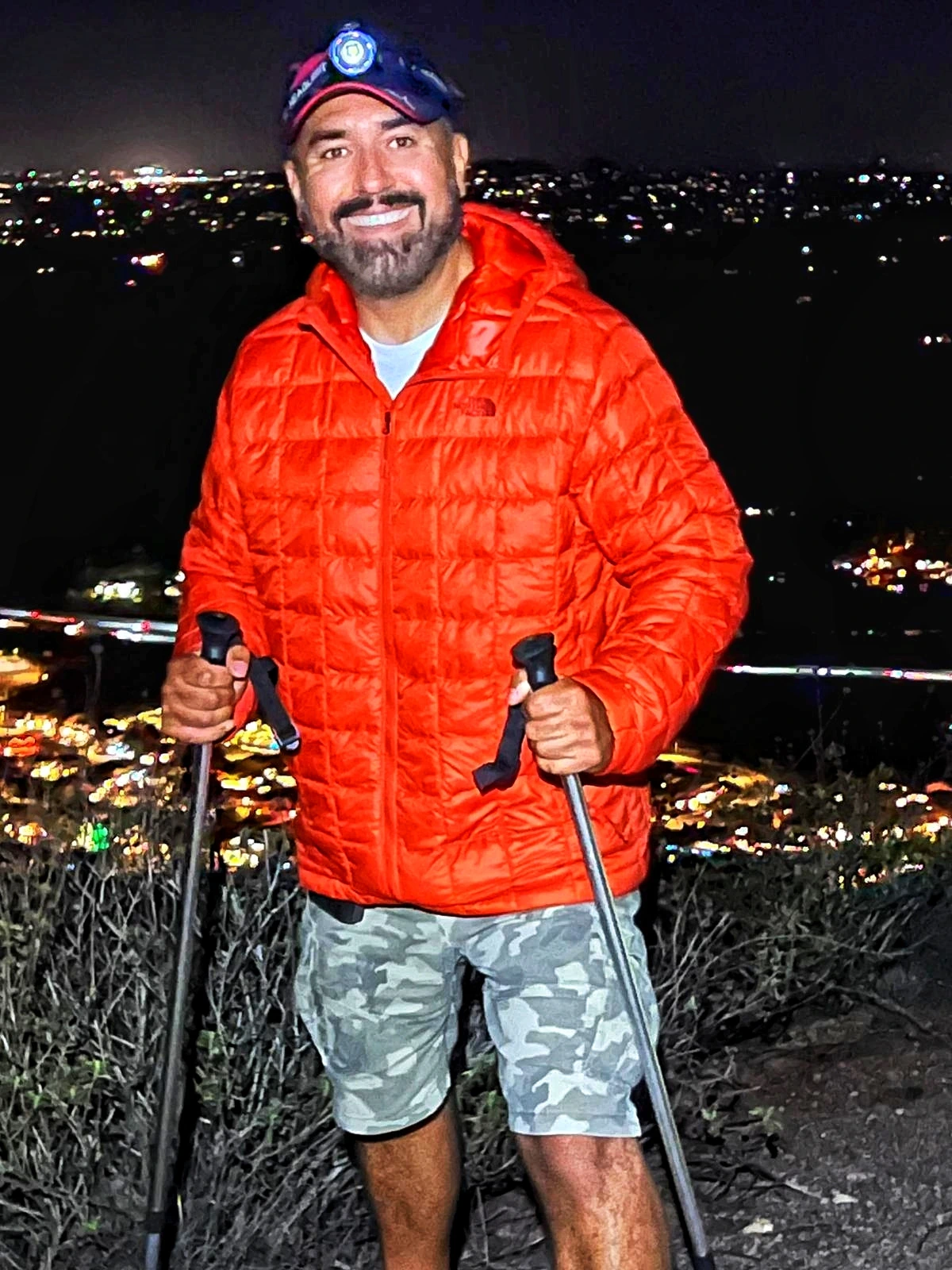 Cazonci Yacata in an orange jacket holding trekking poles above city lights at night