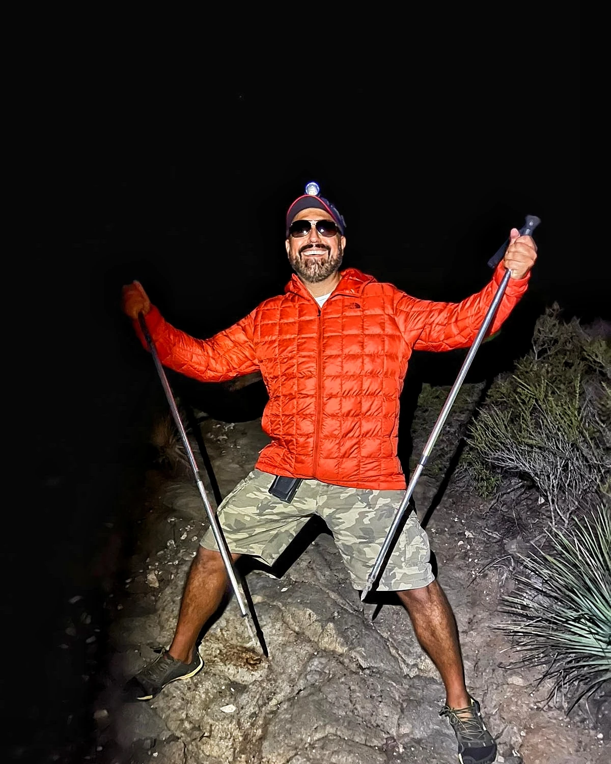 A hiker standing on rocky terrain at night in a bright insulated jacket
