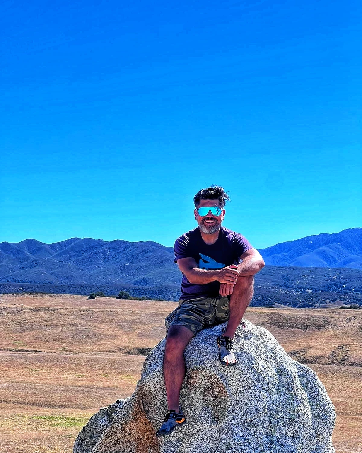 A hiker seated on a boulder beneath a wide blue sky