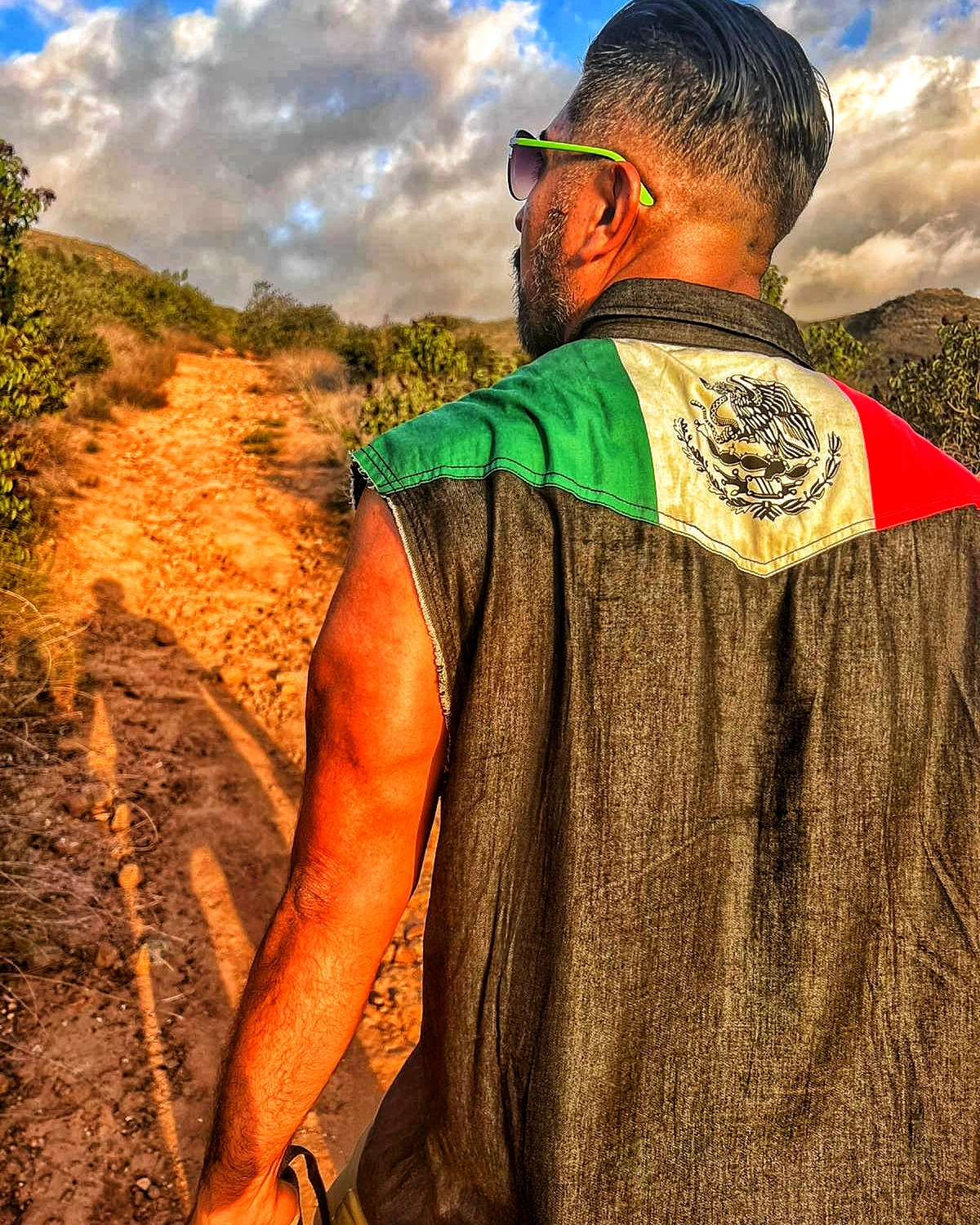 A hiker walking a trail with a Mexican flag panel on a vest