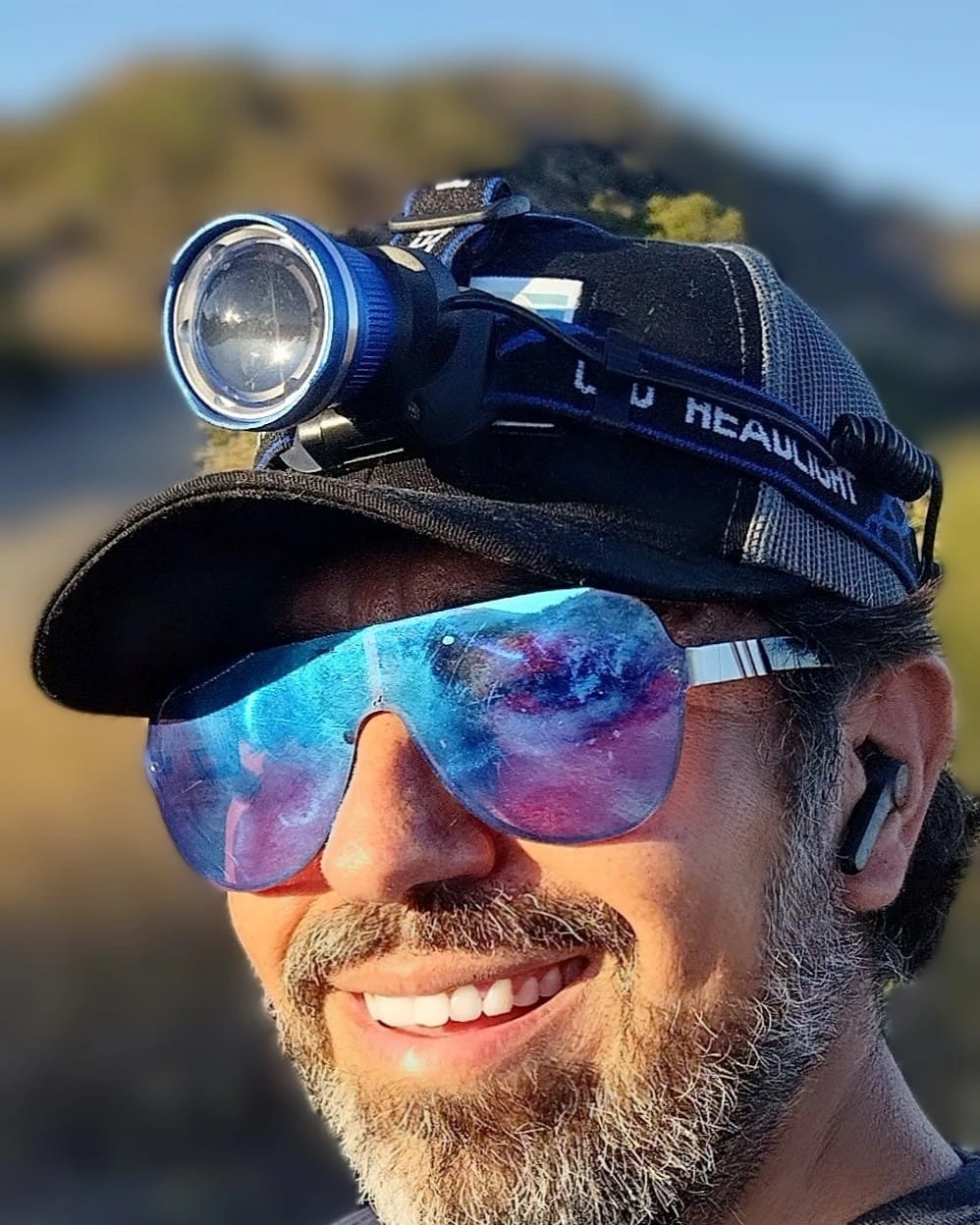 A smiling outdoor portrait wearing reflective sunglasses and a headlamp
